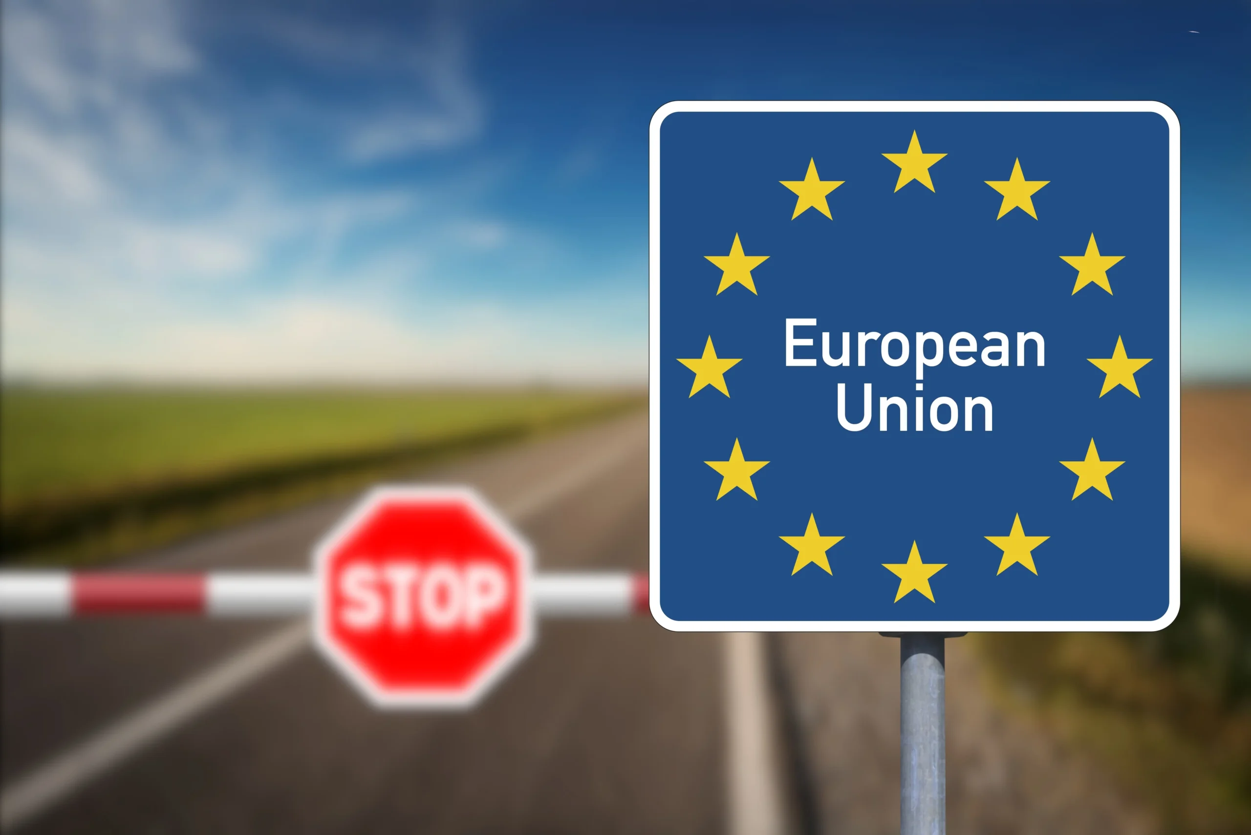 Panneau du drapeau européen devant un poste-frontière avec barrière, illustrant le transit et le dédouanement.