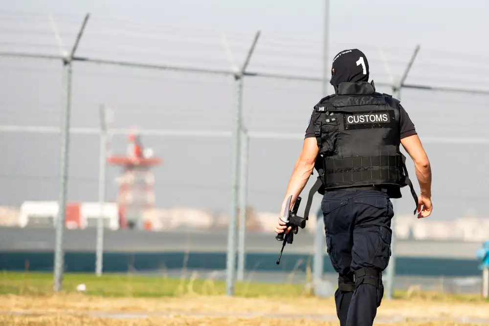 Agent de douane de dos portant un gilet tactique Customs et son équipement professionnel sur un terrain sécurisé.