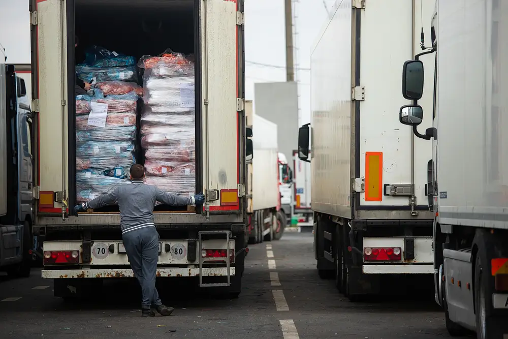 Un douanier inspecte les marchandises à l'arrière d'un camion lors d'un contrôle réglementaire en zone logistique.