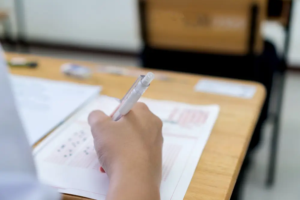 Main d'un candidat remplissant une grille de réponses au stylo lors d'un examen écrit de sélection dans une salle.