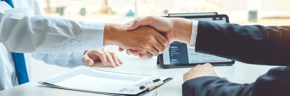 Poignée de main entre un candidat et un jury de recrutement lors d'un entretien d'embauche avec CV sur la table.