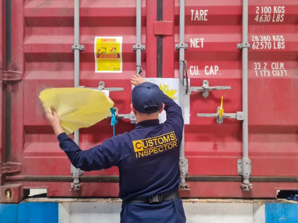 Douanier inspectant un conteneur maritime rouge lors d'un contrôle de marchandises à la frontière.