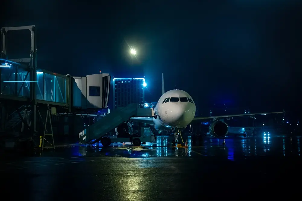 Avion stationné de nuit sur le tarmac éclairé d'un aéroport, illustrant le travail de terrain en shift continu.