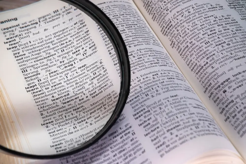 Dictionnaire de langues ouvert sous une loupe, symbolisant l'apprentissage et la préparation aux tests linguistiques.