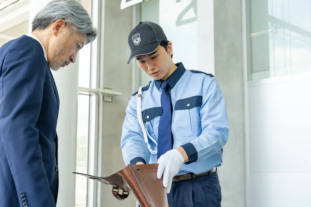 Un douanier en uniforme inspecte le sac d'un voyageur lors d'un contrôle de bagages dans un aéroport.