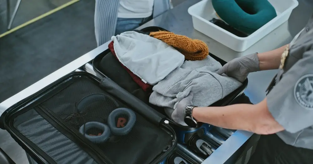 Douanier ganté inspectant le contenu d'une valise ouverte lors d'un contrôle de bagages à l'aéroport.