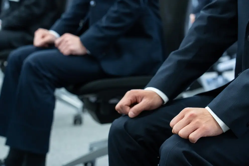 Candidat stressé en costume attendant son entretien, les mains nerveusement crispées sur ses genoux.