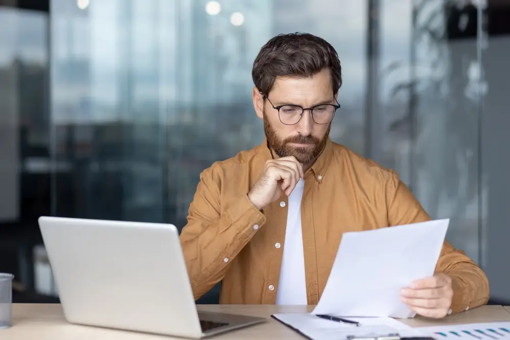 Jeune professionnel concentré étudiant des documents de compétences devant son ordinateur portable.