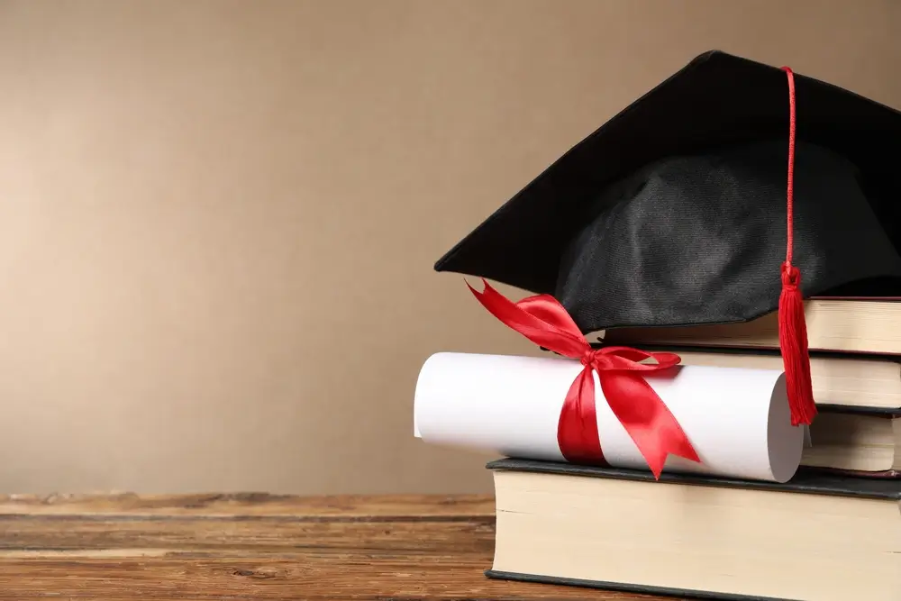 Toque de graduation et diplôme avec ruban rouge sur une pile de livres, symbolisant la validation d'une qualification.
