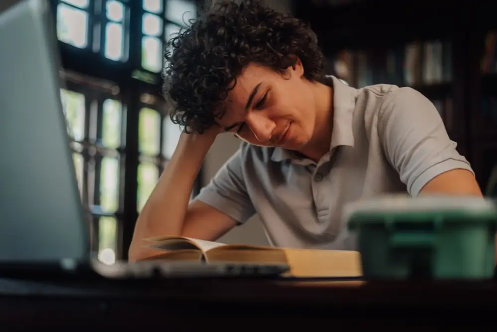 Candidat préparant un test SELOR avec un livre et un ordinateur portable sur son bureau d'étude.