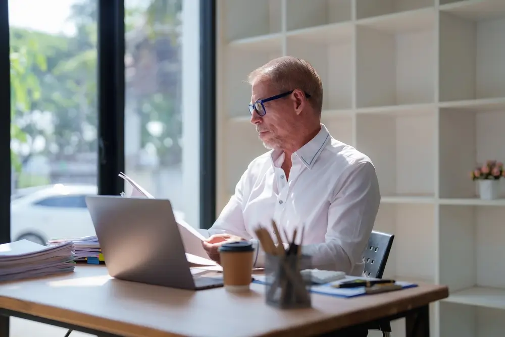 Employé de bureau administratif fédéral analysant des dossiers de screening devant son ordinateur portable.