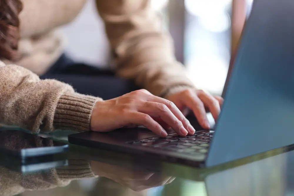 Mains d'un candidat utilisant un ordinateur portable sur un bureau pour s'inscrire en ligne à des tests d'évaluation.