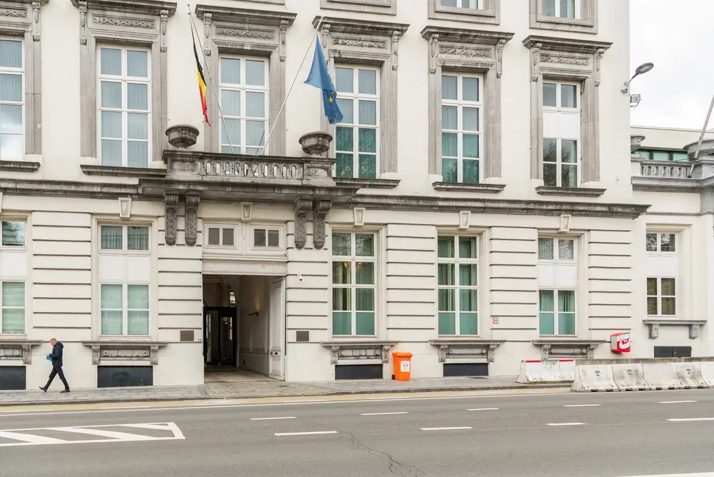 Façade d'un bâtiment administratif belge avec les drapeaux de la Belgique et de l'Union européenne devant l'entrée.