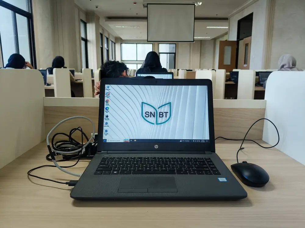 Écran d'ordinateur affichant l'interface d'un test en ligne sur un bureau de salle d'examen avec d'autres candidats.