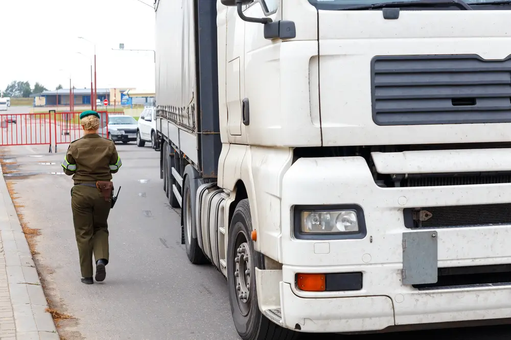 Agente en uniforme marchant à côté d'un camion blanc pour une mission de surveillance et de patrouille douanière.